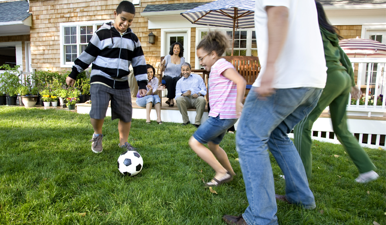 Image of a family playing soccer in a yard