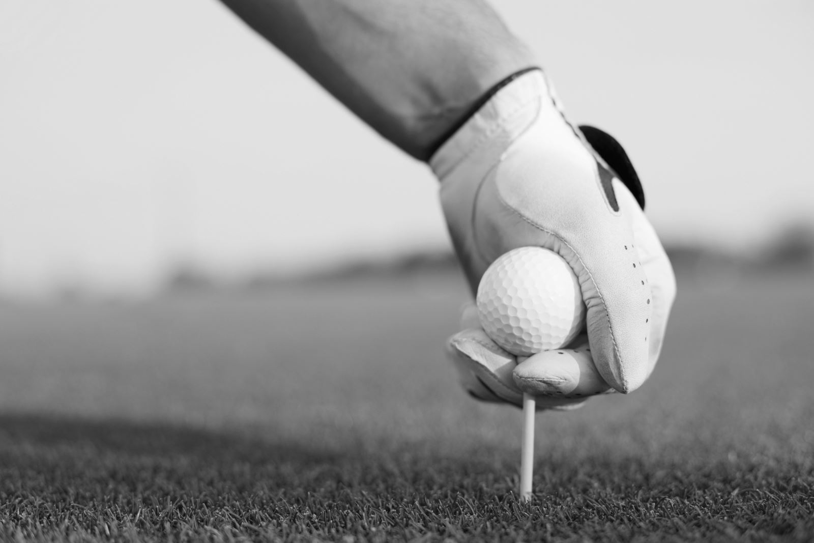 Black and white image of a man putting a golf ball and tee in the ground