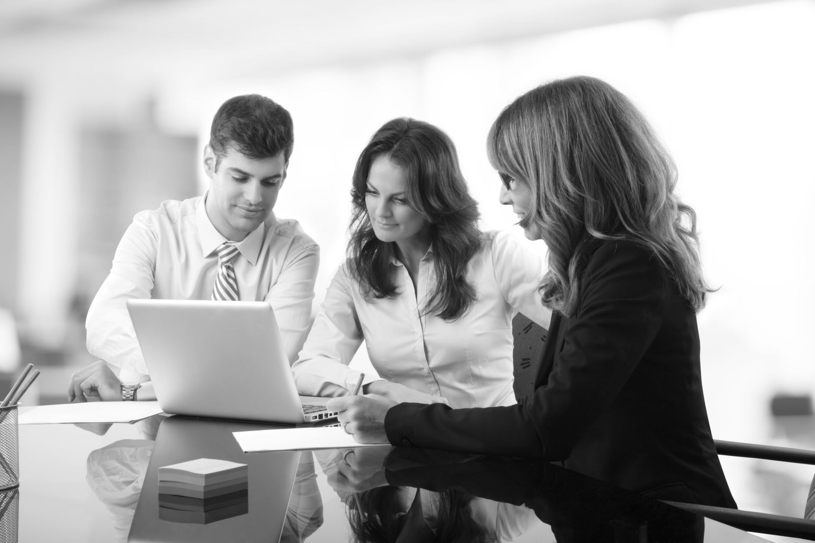 Black and white image of two business women and a business man looking at a laptop