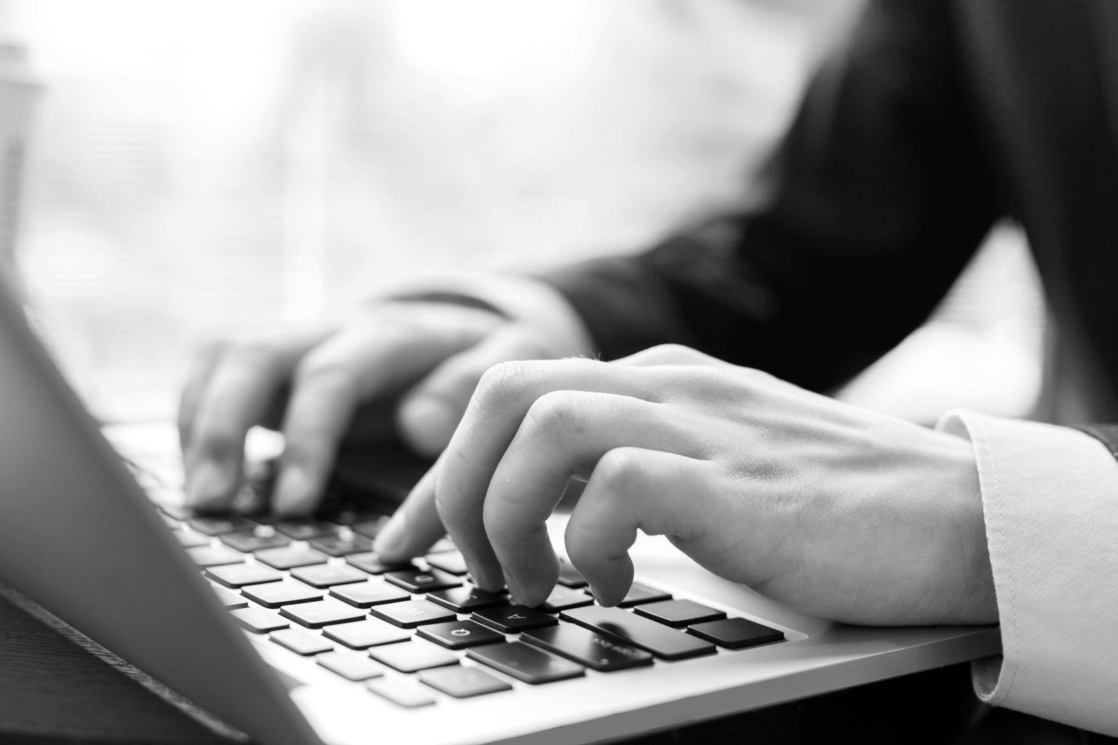 Black and white image of a man typing on a laptop